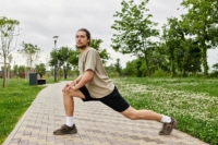 Ein sportlicher, junger Mann dehnt sich in einem Park