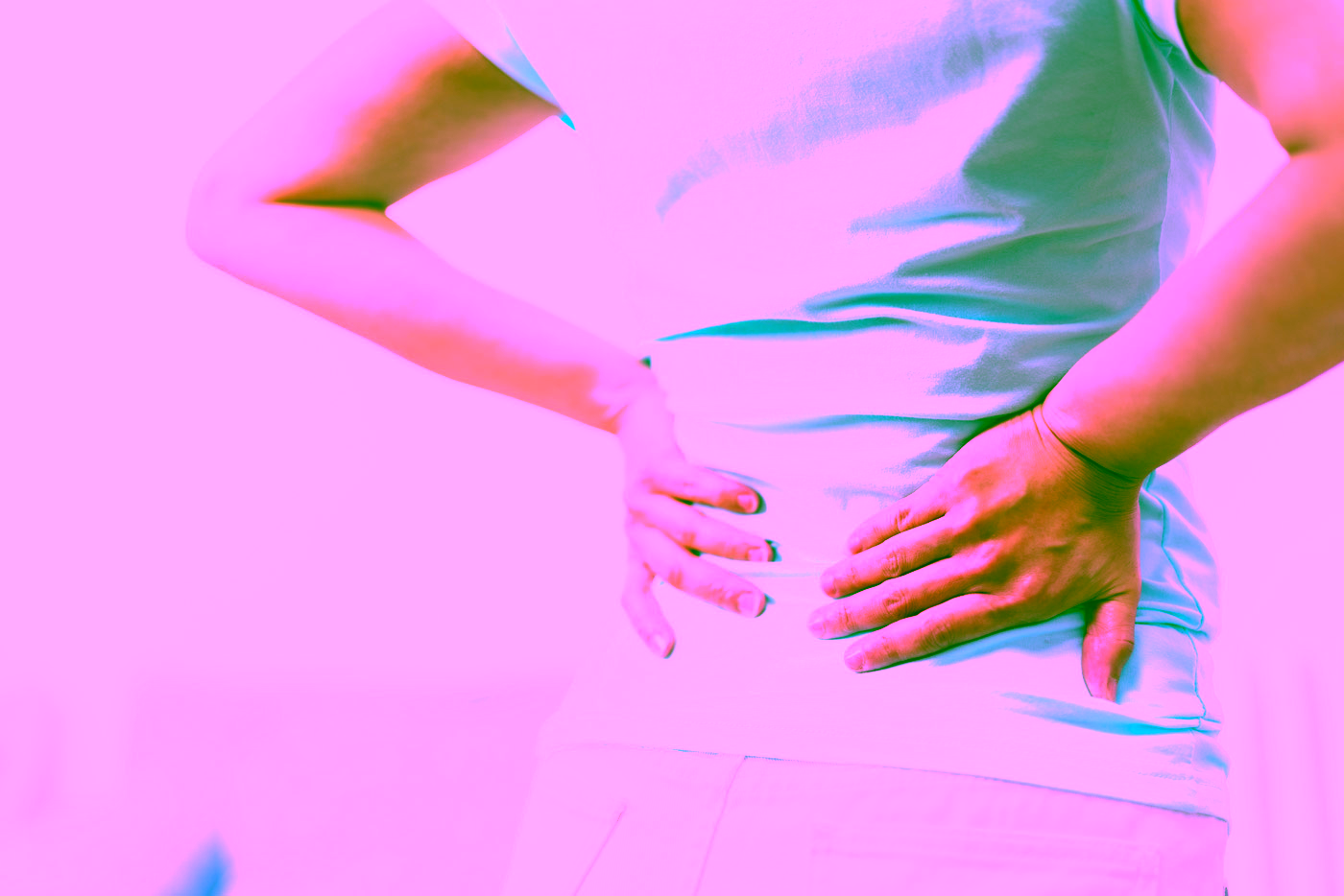 Frau hält sich die Hände an den unteren Rücken, ein typischer Fall für eine Schmerztherapie in der Orthopädie